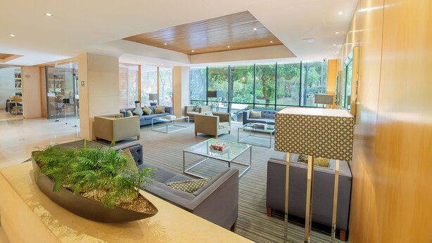 Un vestíbulo amplio con mobiliario moderno, ventanas grandes que ofrecen vista a zonas verdes y una decoración floral central.