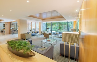Un vestíbulo amplio con mobiliario moderno, ventanas grandes que ofrecen vista a zonas verdes y una decoración floral central.