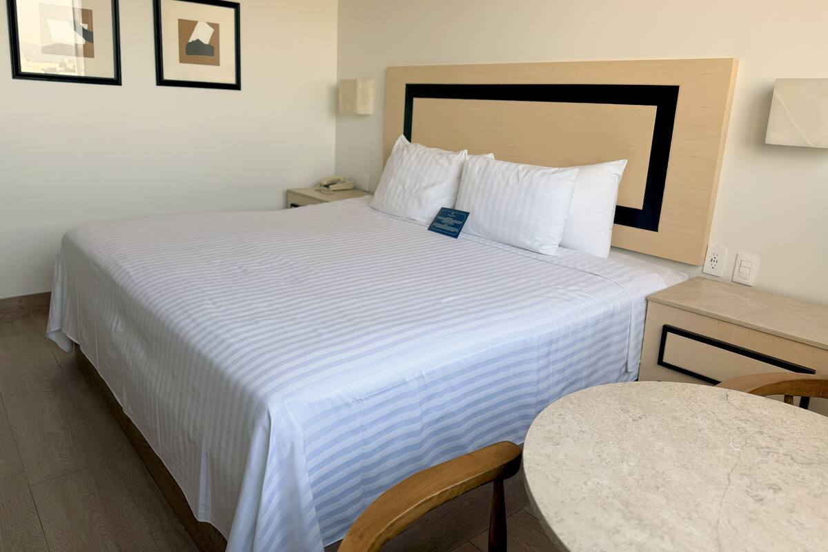 A hotel room with a large bed, a bedside table, a chair, and a small round table.