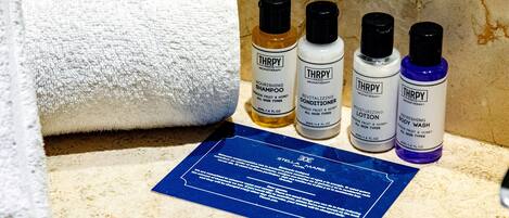 Un baño con una toalla blanca, cuatro botellas de productos capilares THRPY y una tarjeta informativa azul sobre el mostrador.