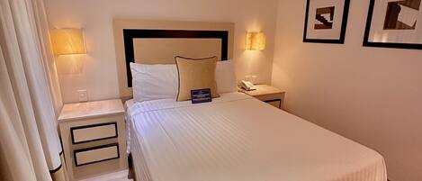 Una habitación de hotel con una cama grande, dos mesitas de noche, una cabecera y dos lámparas fijadas a la pared.