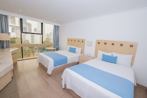 Habitación de hotel con dos camas, un escritorio y vistas a la ciudad.