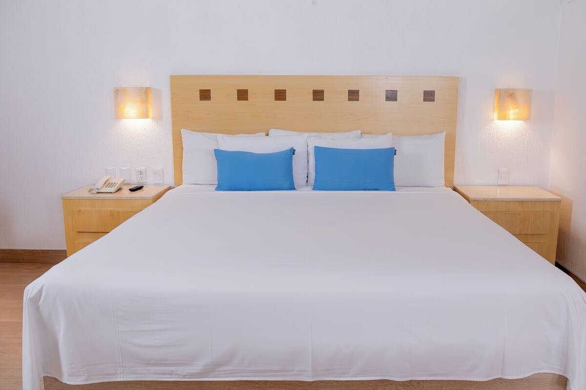 A neatly made bed with white bedding and two blue pillows, flanked by wooden nightstands with lamps and a phone.
