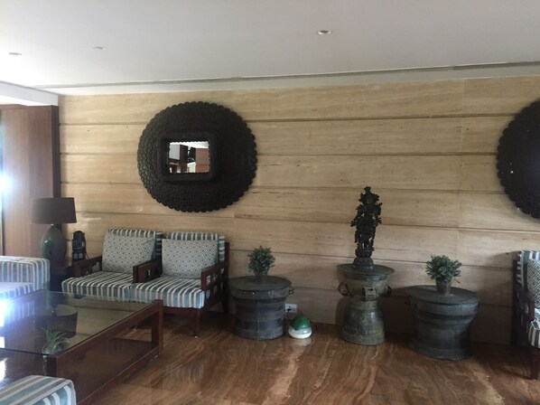 A living room with a sofa, armchairs, a coffee table, and decorative items including a mirror, a statue, and potted plants. - Madhubhan Resort & Spa (Anand)