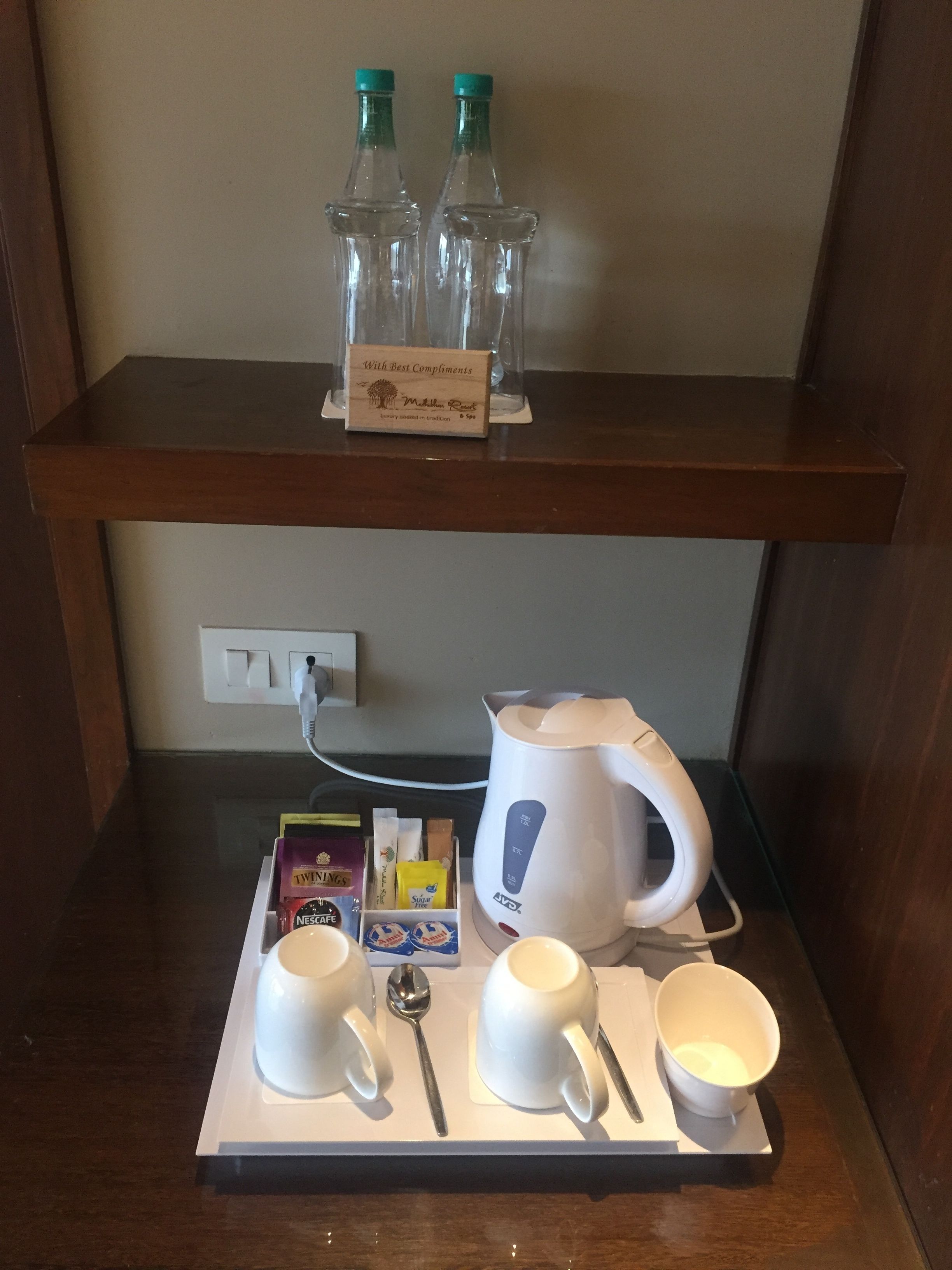 A breakfast tray with coffee cups, a spoon, a bowl, and a kettle on a wooden table.