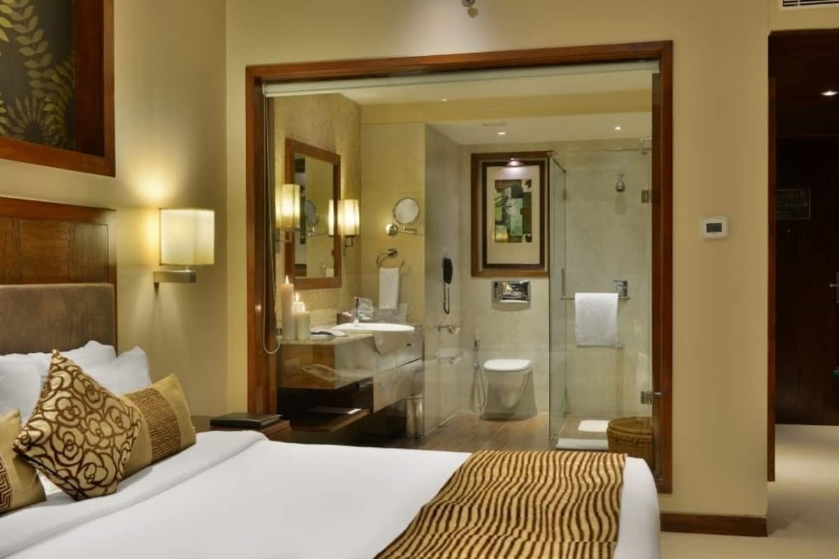 Une chambre d’hôtel dotée d’un grand lit, d’une salle de bain avec une douche à parois de verre et d’une porte en bois donnant accès à la salle de bain.
