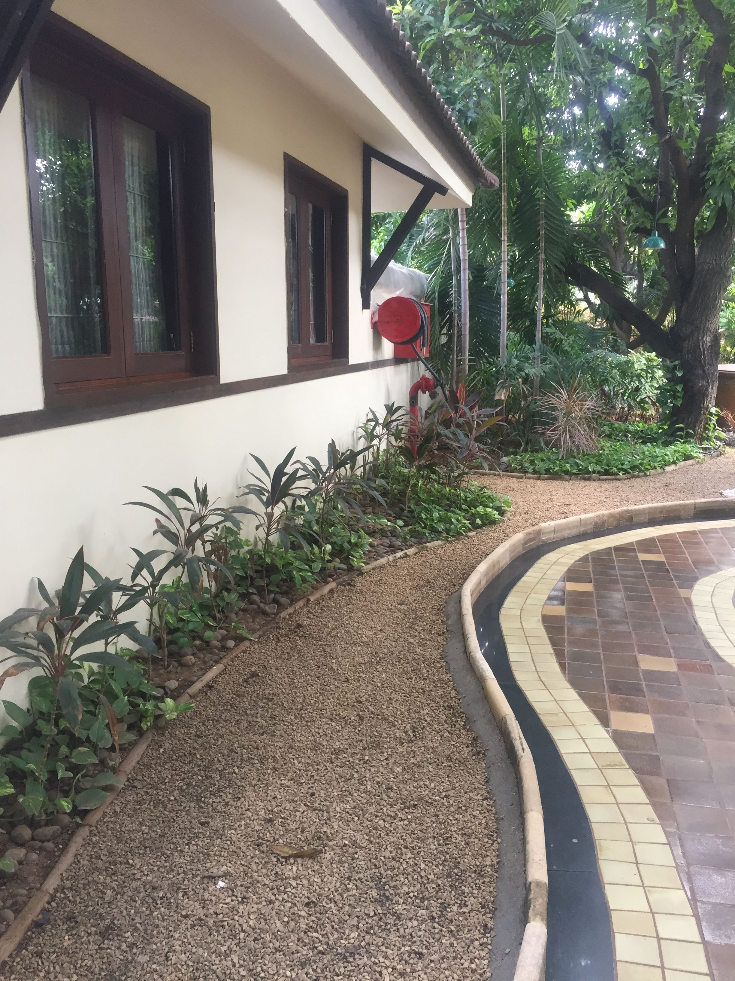 A building with a tiled patio area, a gravel pathway, and various plants.