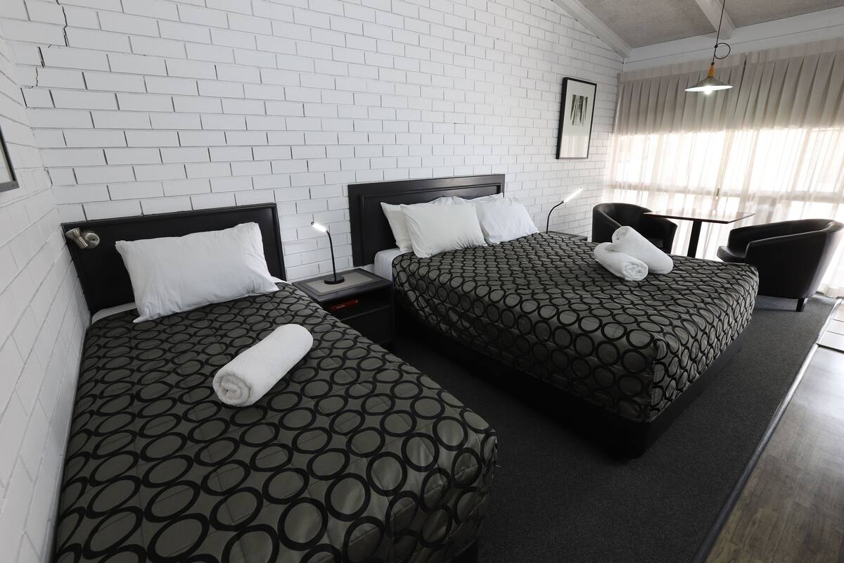 A hotel room with two beds, a nightstand, a chair, and a window with curtains.