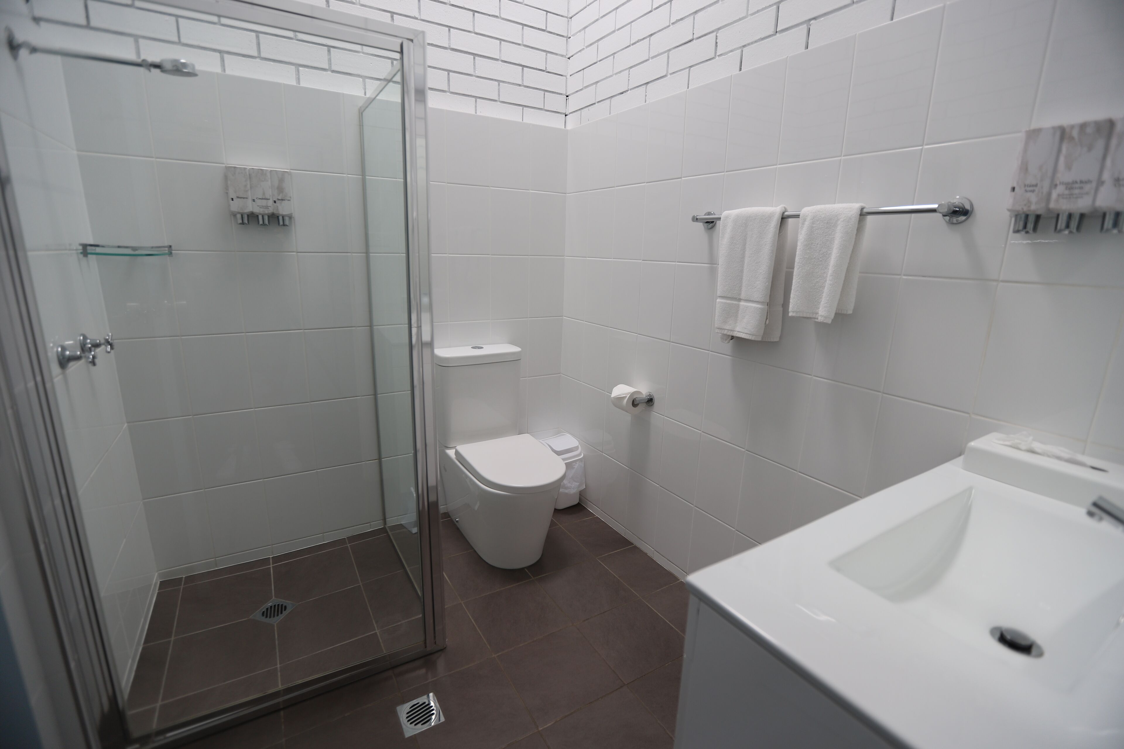 A bathroom with a glass shower enclosure, a toilet, a sink, and a towel rack with towels.