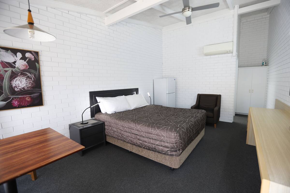 A bedroom with a bed, a desk, a chair, a nightstand, and a ceiling fan.
