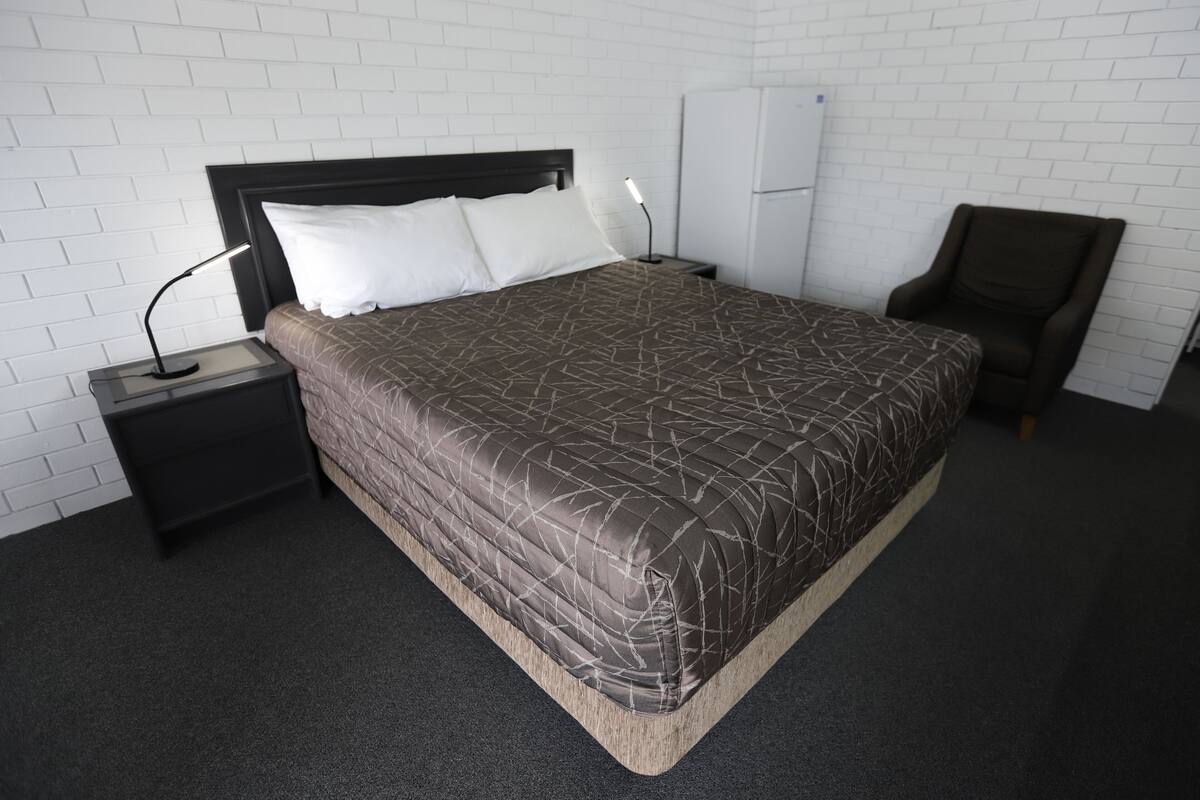 A neatly arranged hotel room with a large bed, a nightstand, a chair, and a white wardrobe.