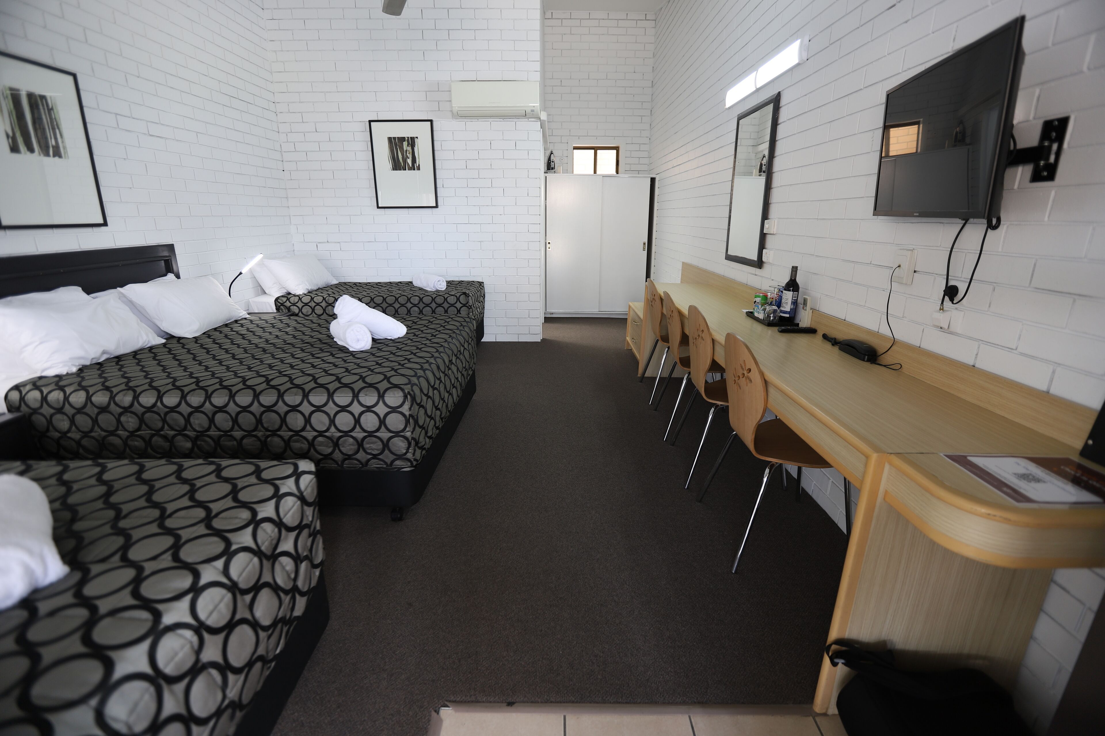 Een hotelkamer met twee bedden, een bureau, stoelen, een televisie en een kledingkast.