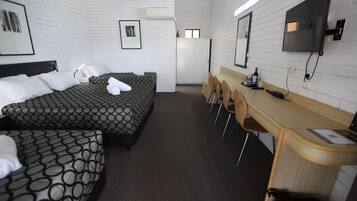 Een hotelkamer met twee bedden, een bureau, stoelen, een televisie en een kledingkast.