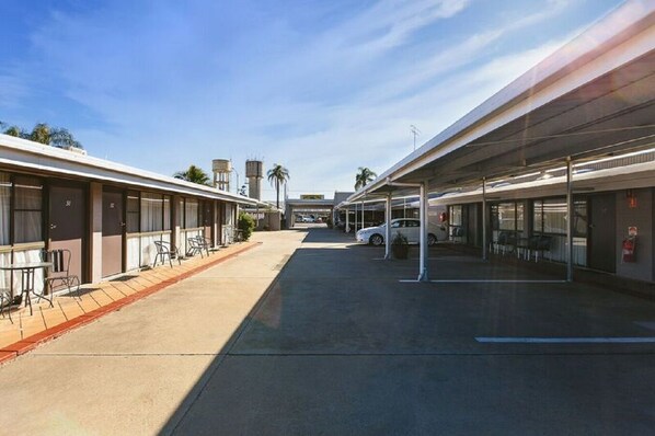 A motel with a covered parking area, individual rooms with windows, and a clear sky.