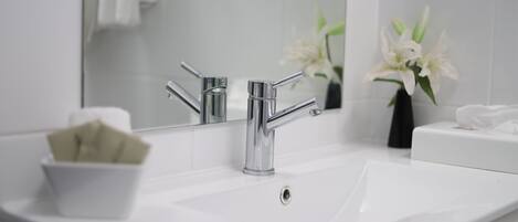 A modern bathroom with a chrome faucet, a white sink, and a mirror reflecting a towel and a vase of white flowers.