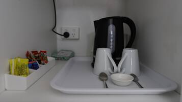 Een witte dienblad met een waterkoker, twee witte kopjes, een lepel en een kom. Links liggen suikerzakjes en theezakjes.