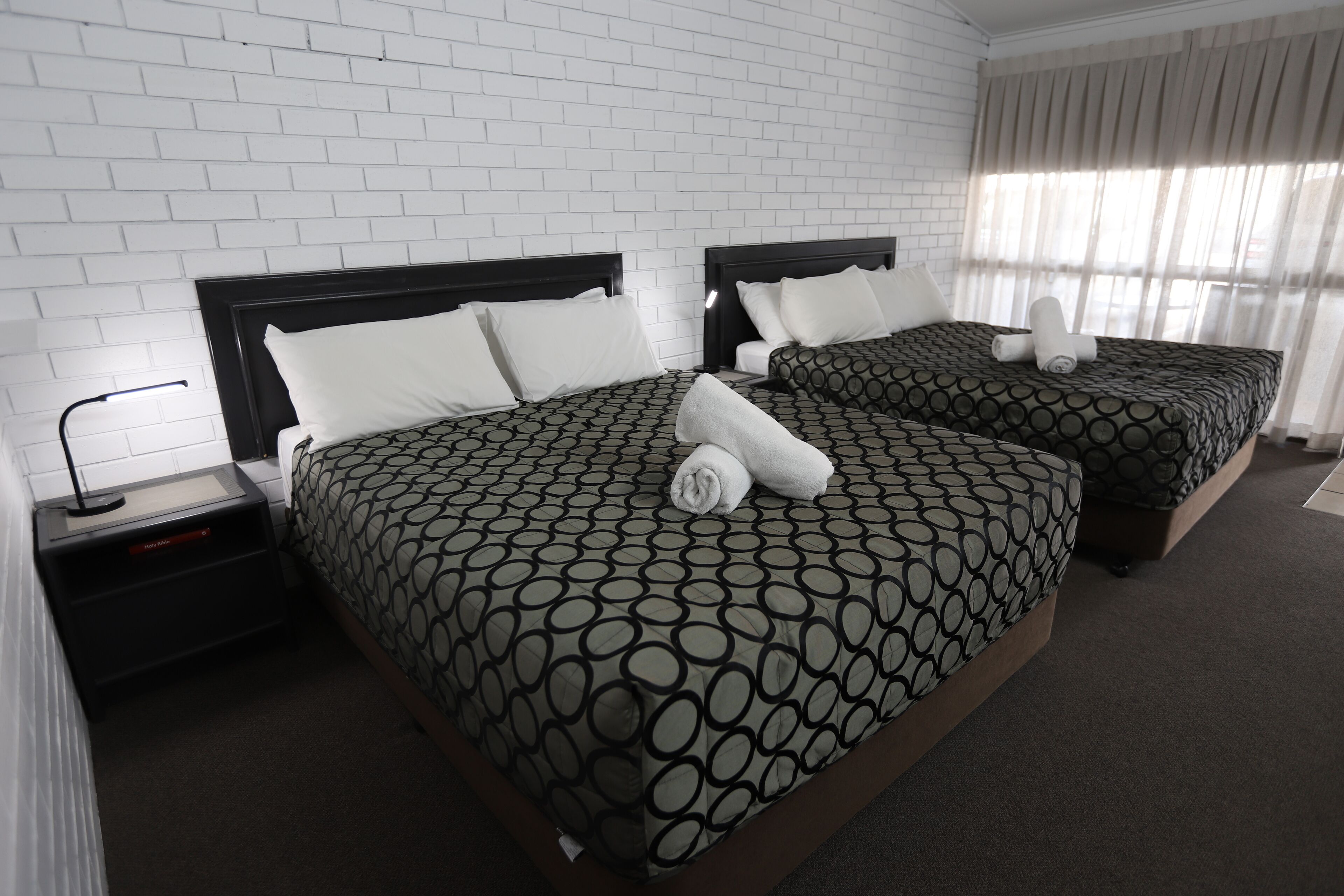 Habitación de hotel con dos camas, paredes de ladrillo blanco y un ventanal con cortinas translúcidas.