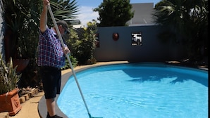 A person cleaning a swimming pool with a long-handled tool.
