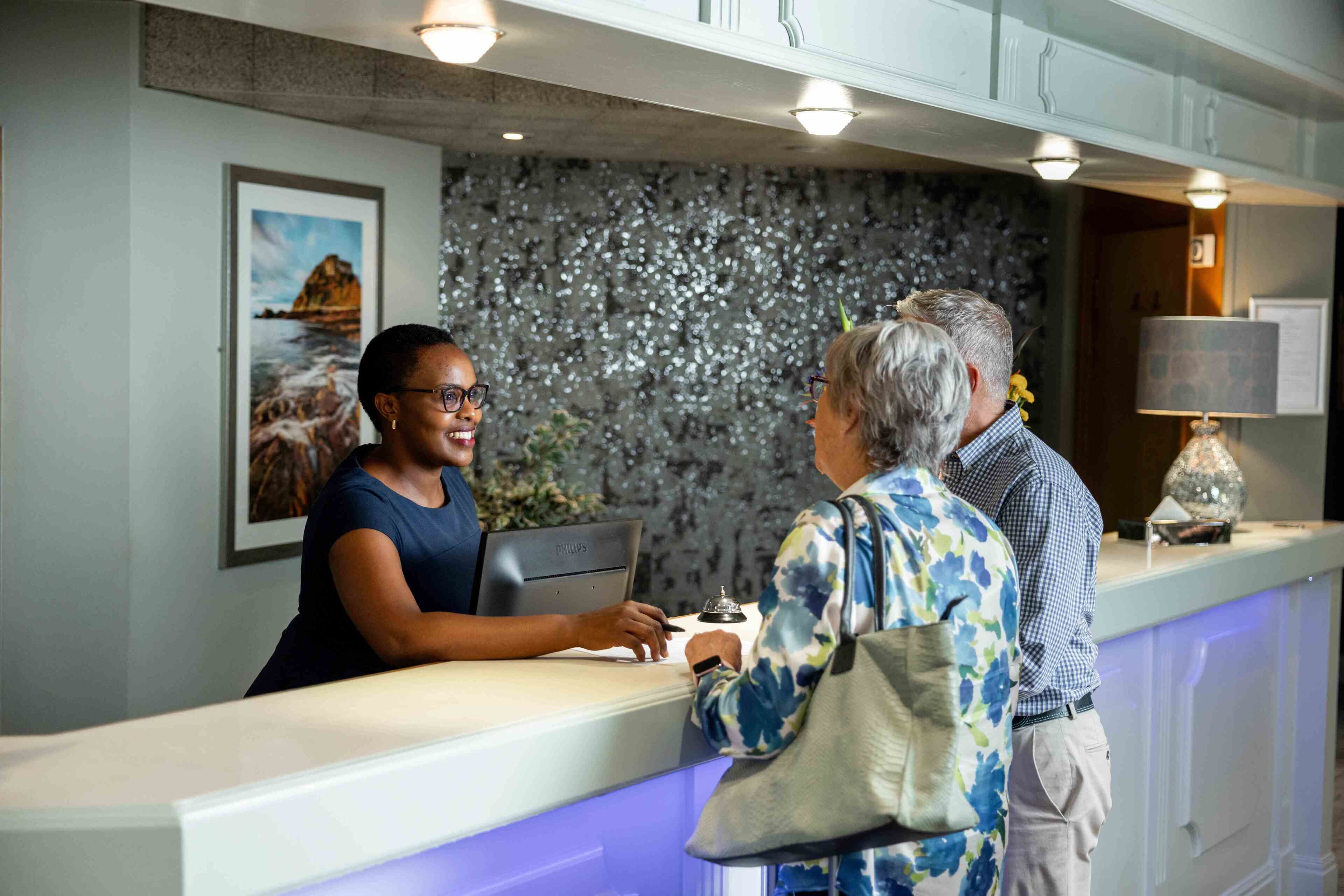 A reception desk with a digital screen, a framed landscape painting, and a textured wall.