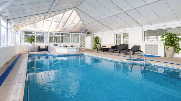 An indoor swimming pool with a glass ceiling, lounge chairs, and potted plants. - The Monterey Hotel, BW Signature Collection (St. Saviour)