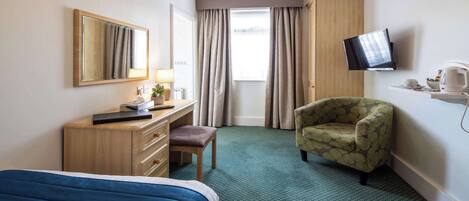 Una habitación de hotel con cama, escritorio con lámpara, silla, televisión y ventana con cortinas.