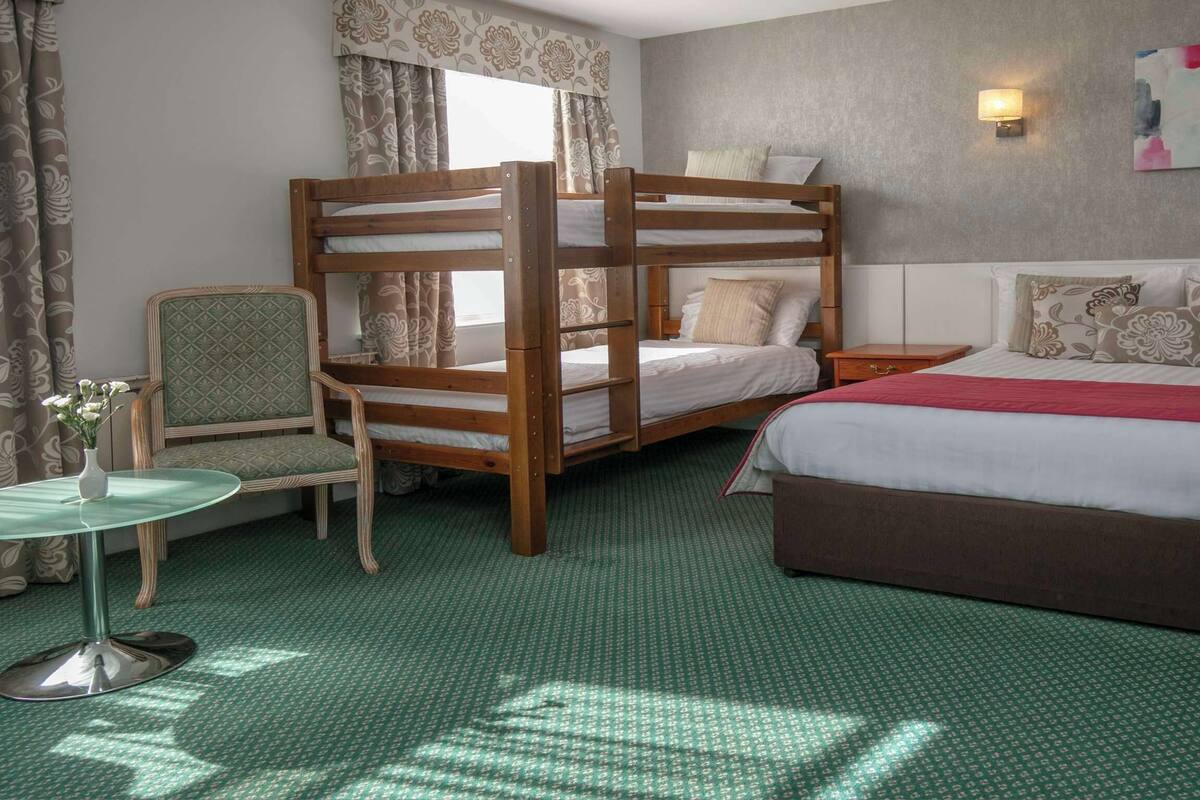 A room with bunk beds, a single bed, a chair, a small table, and a lamp.