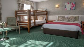 Una habitación con literas, una cama individual, una silla, una mesita y una lámpara.