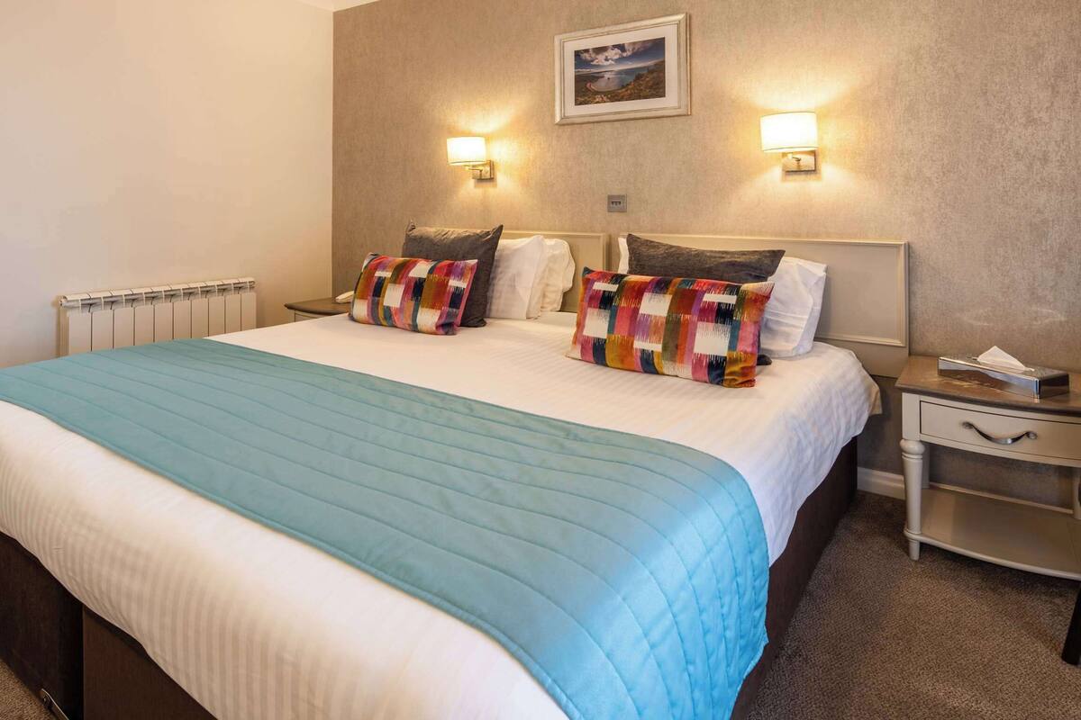 A hotel room with a large bed, two bedside lamps, a nightstand, and a chair.