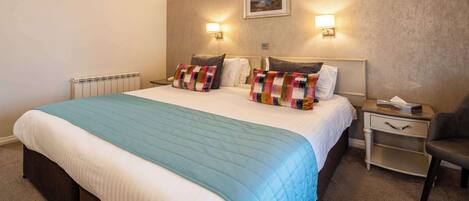 Una habitación de hotel con una cama grande, dos lámparas de noche, una mesita de noche y una silla.
