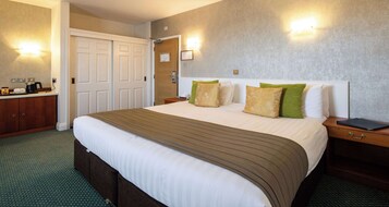 Habitación de hotel con una cama grande, una mesita de noche, un armario y una lámpara fijada a la pared.