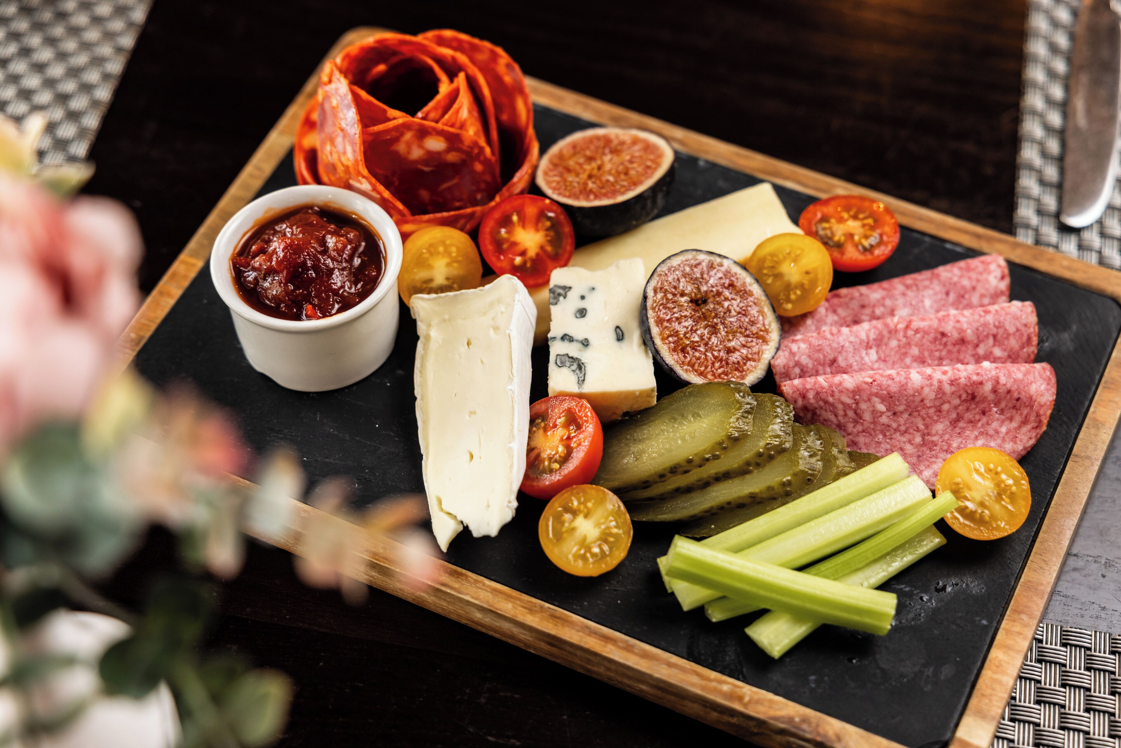 A charcuterie board with various cheeses, meats, and vegetables on a slate board.