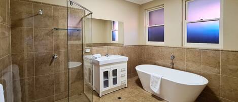 A bathroom with a glass-enclosed shower, a freestanding bathtub, a sink, and a mirror above the sink.