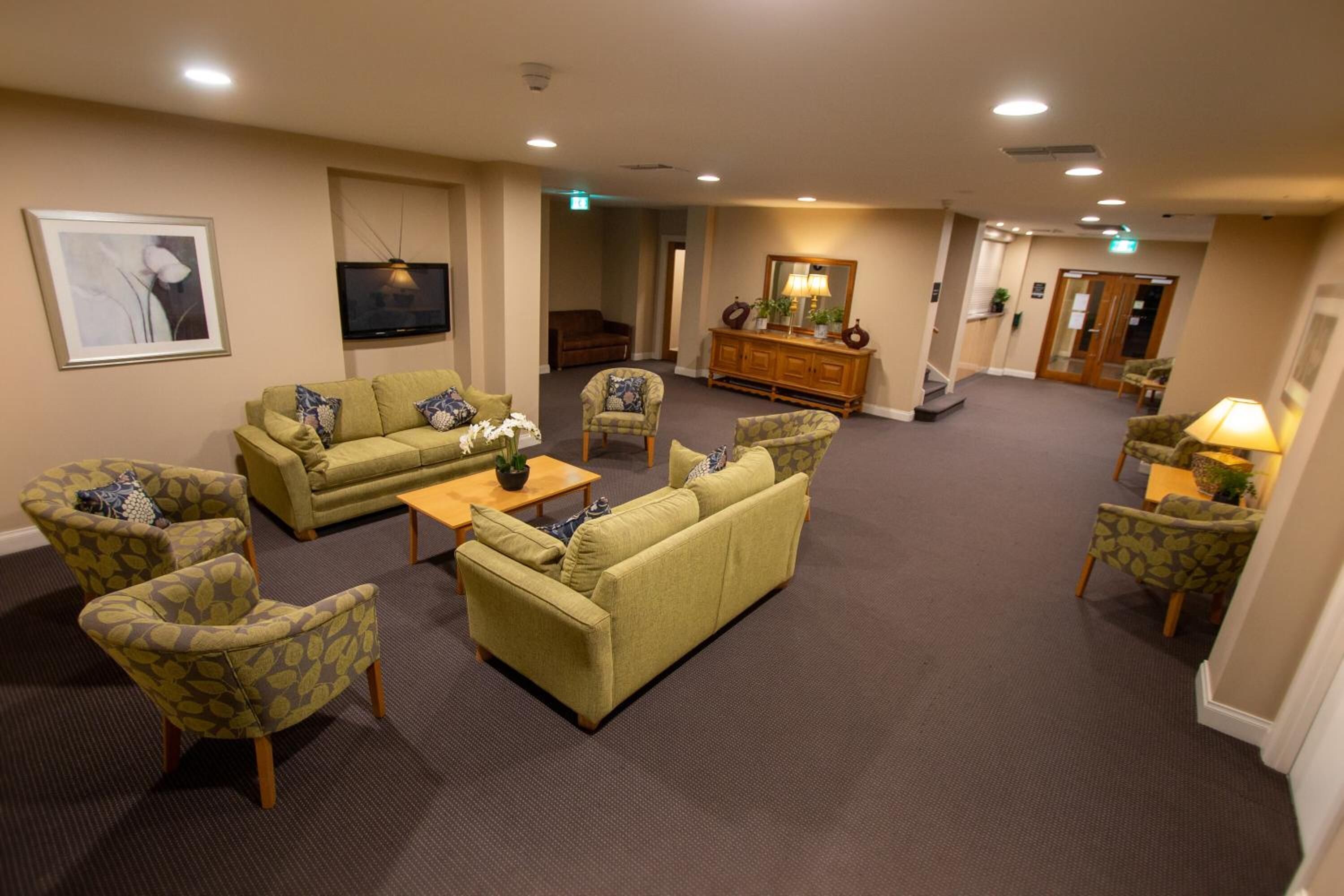 A hotel lounge with sofas, armchairs, a coffee table, a television, and a mirror.