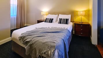 A neatly made bed with a grey blanket, two bedside tables with lamps, and a window with curtains.