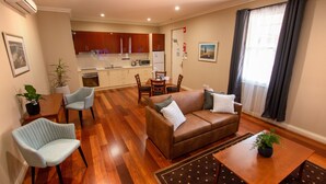 Una sala moderna con un sofá marrón, dos sillones, una mesa de comedor y una cocina al fondo.