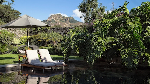 A pool area with lounge chairs and an umbrella, surrounded by lush greenery and a mountain backdrop. - Hotel Boutique Casa Fernanda - Adults only (Tepoztlán)