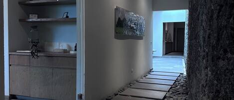 Un pasillo con un sendero de piedra, una zona de cocina con estanterías de madera y un cuadro en la pared.
