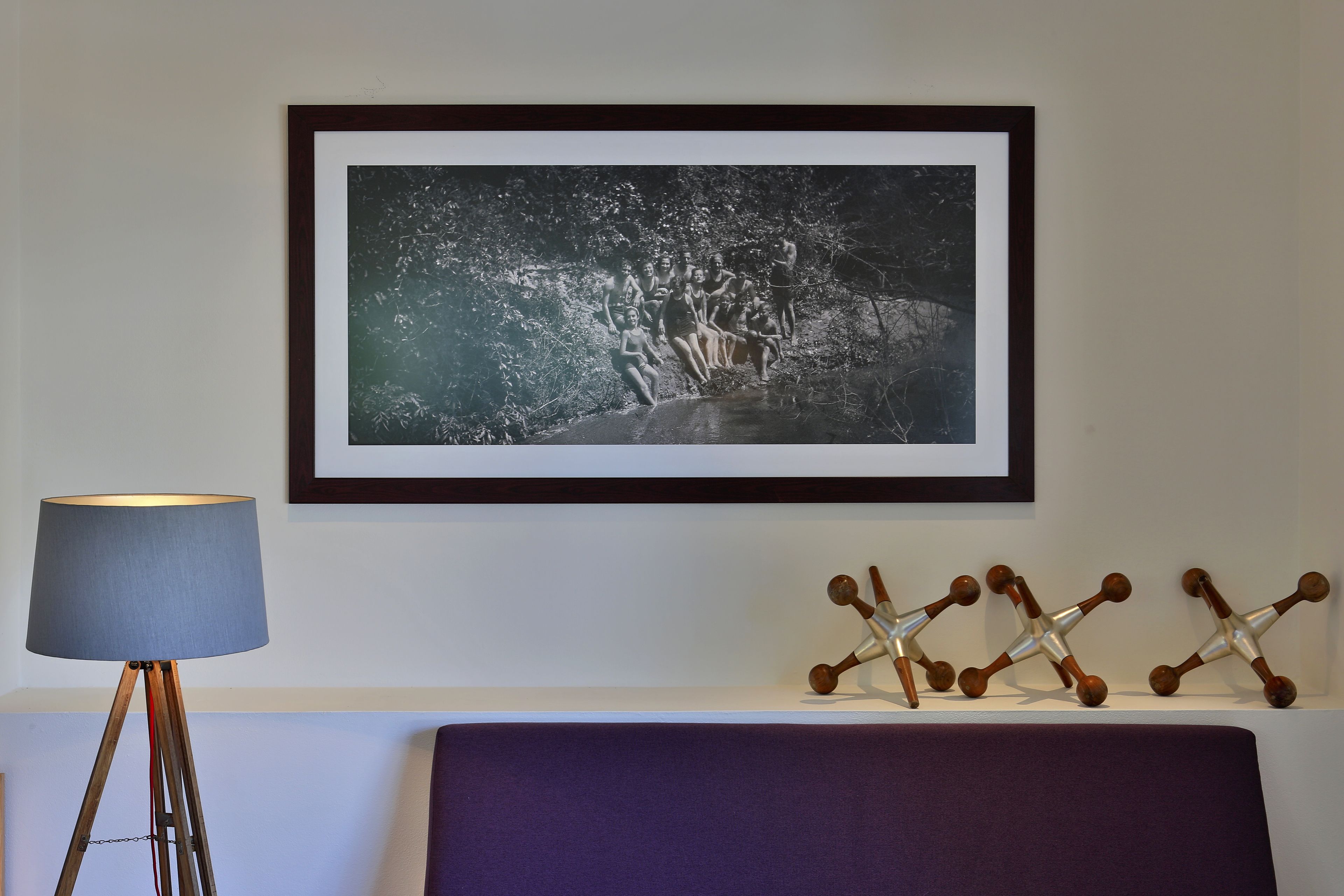 A framed photograph of a group of people in a natural setting, a floor lamp, and decorative wooden sculptures on a shelf.