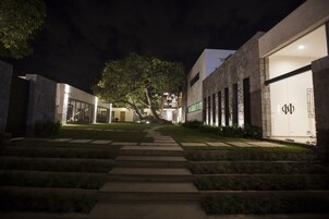 A nighttime view of a modern building with a well-lit entrance, a stone facade, and a clear pathway leading to the entrance.
