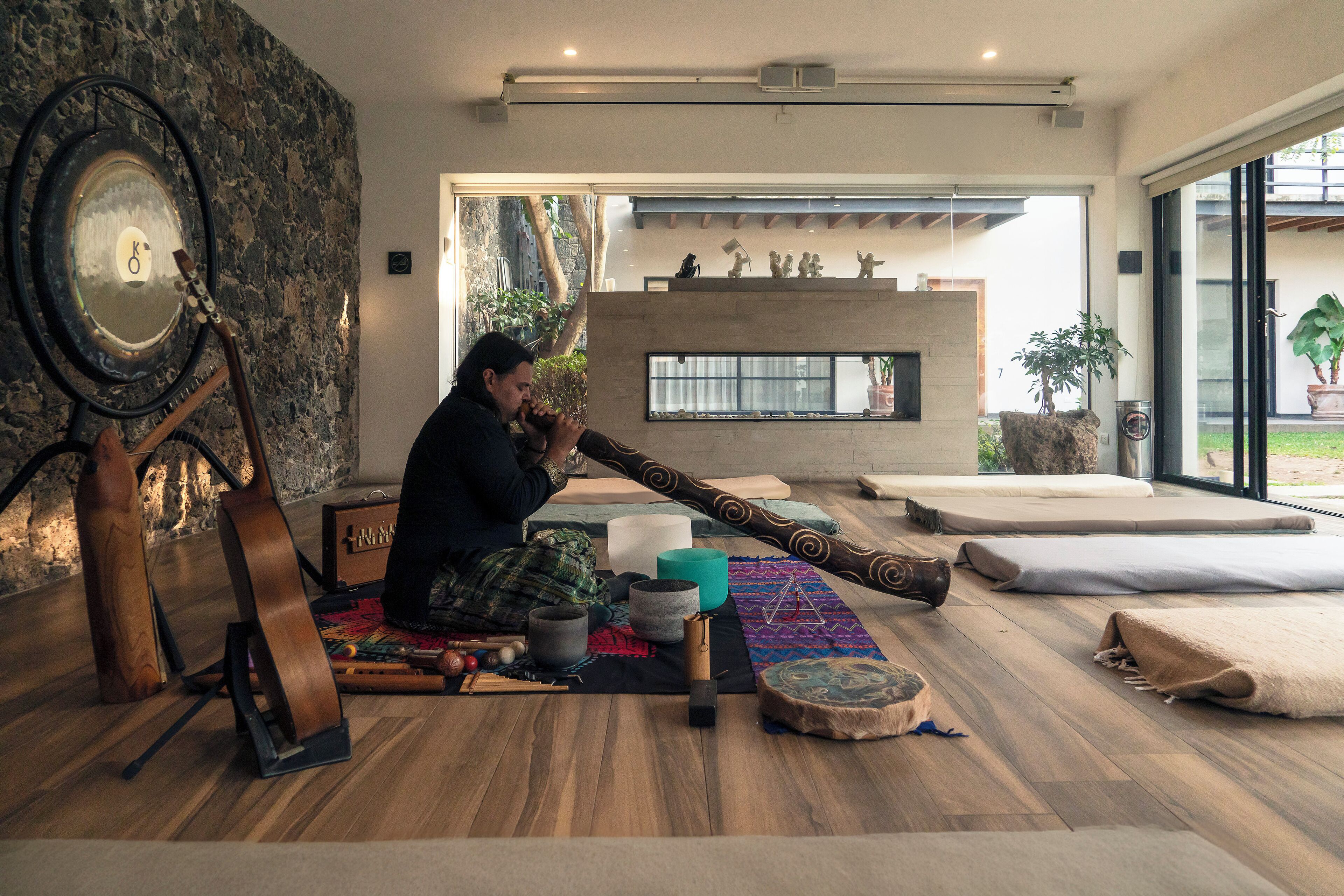 Um quarto com parede de pedra, um espelho grande, uma guitarra, um tambor e uma lareira.