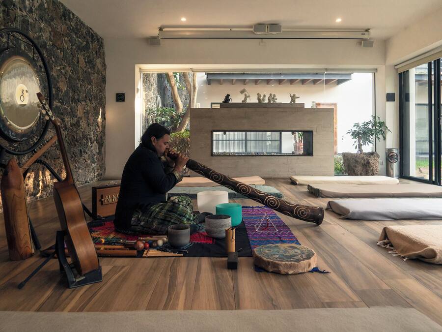Um quarto com parede de pedra, um espelho grande, uma guitarra, um tambor e uma lareira.