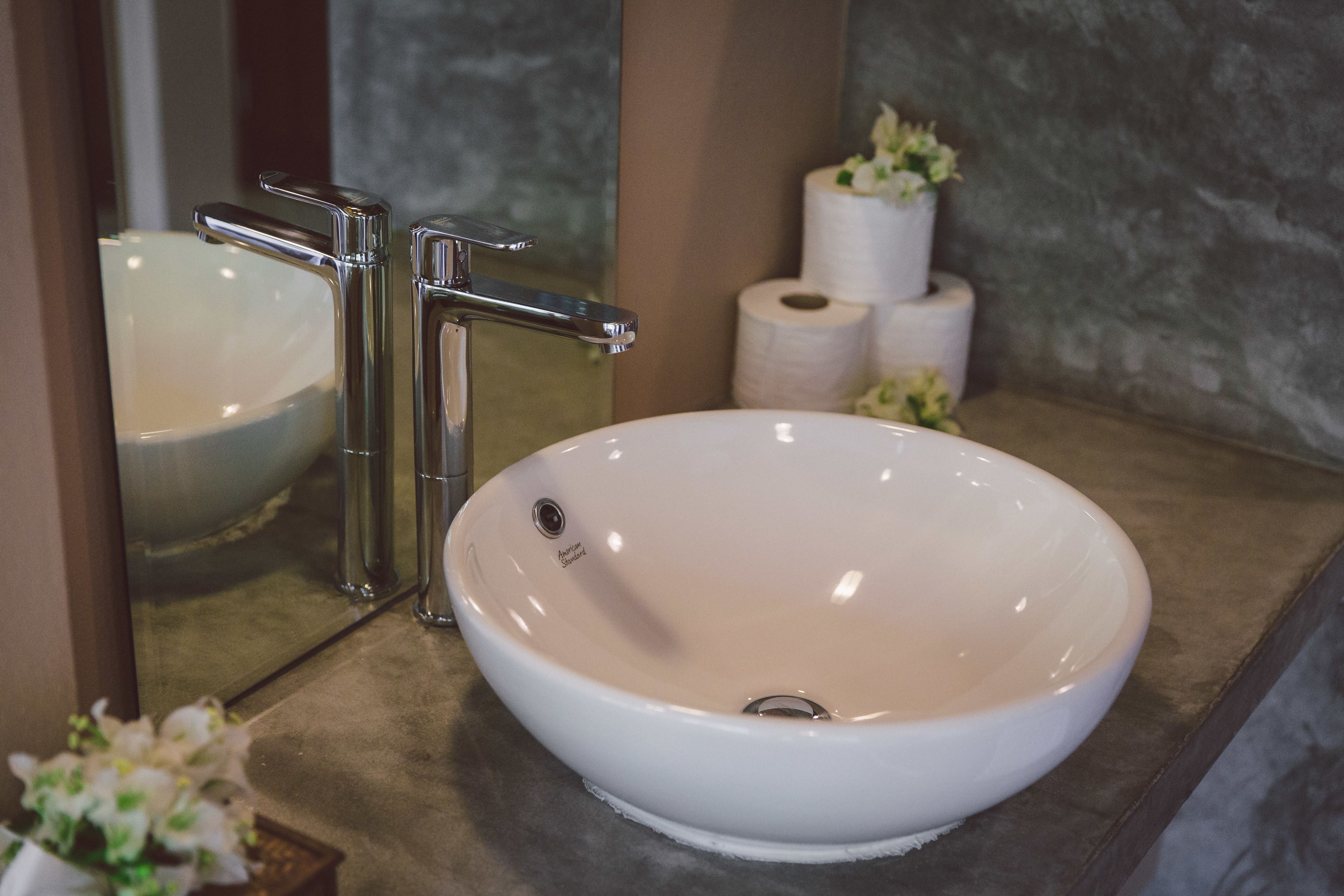 A bathroom with a white sink, chrome faucet, and a mirror reflecting the sink and toilet paper.