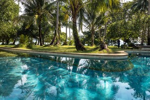 Piscina cristalina rodeada de abundante vegetación y palmeras.