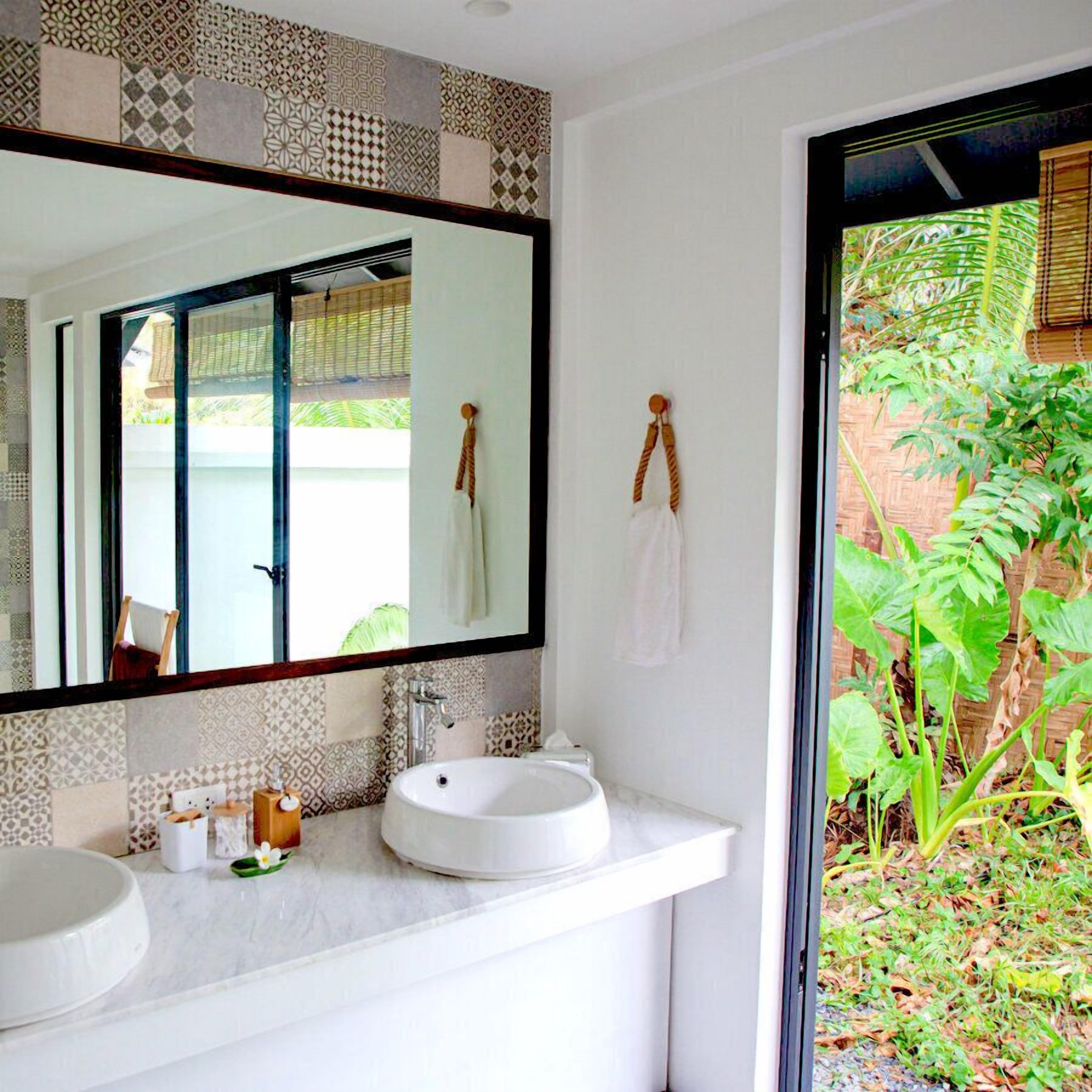 Un baño con un espejo grande, dos lavamanos y vistas a la vegetación exterior.