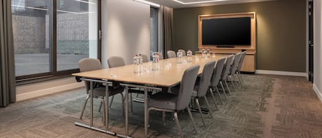 A conference room with a long table, chairs, a projector screen, and a carpeted floor.