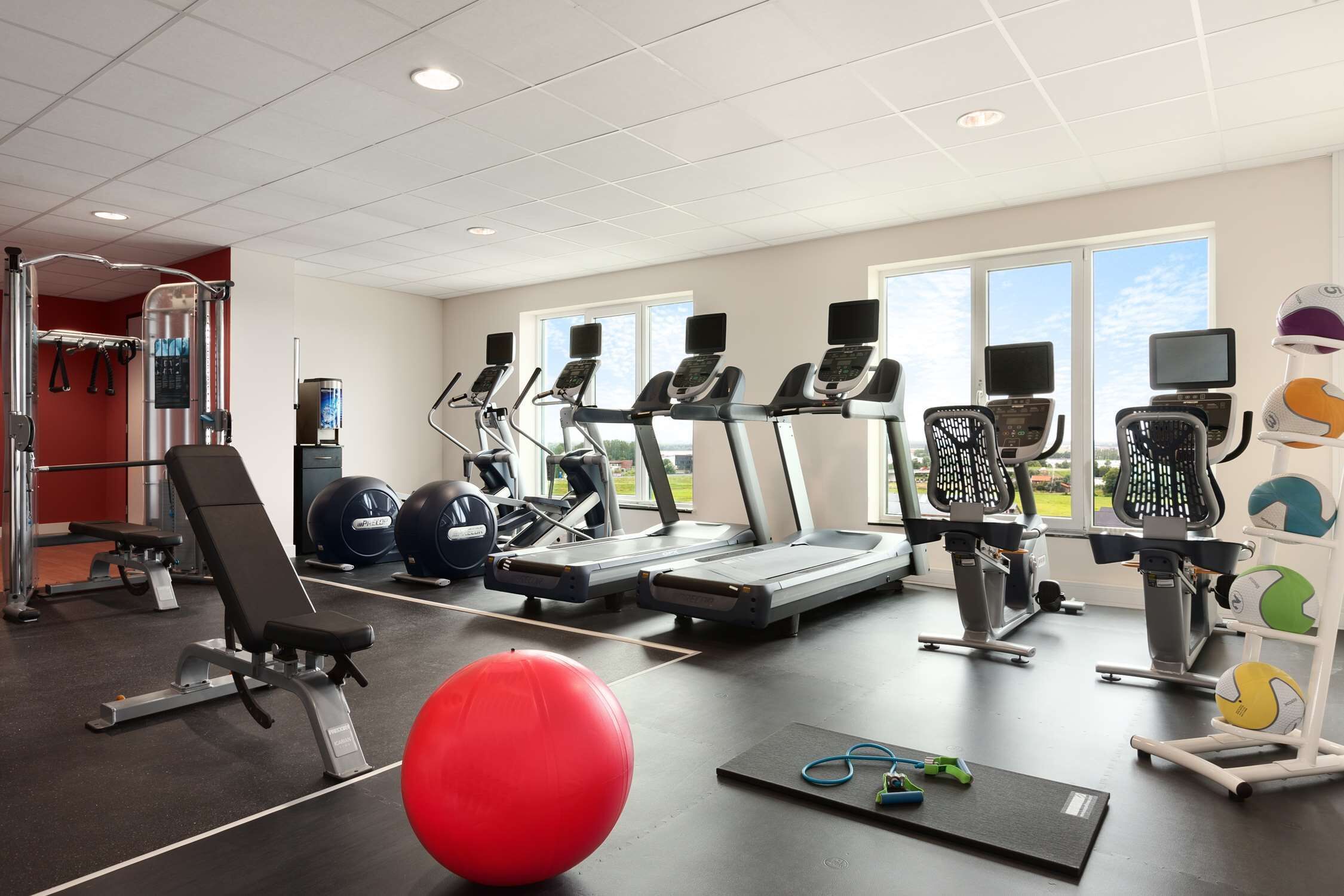 Een sportschool met loopbanden, elliptische trainers, een rode fitnessbal en een roeimachine.