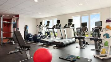 Een sportschool met loopbanden, elliptische trainers, een rode fitnessbal en een roeimachine.