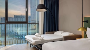 Ein Hotelzimmer mit zwei Betten, einem großen Fenster, Blick auf die Stadt und einer modernen Lampe.