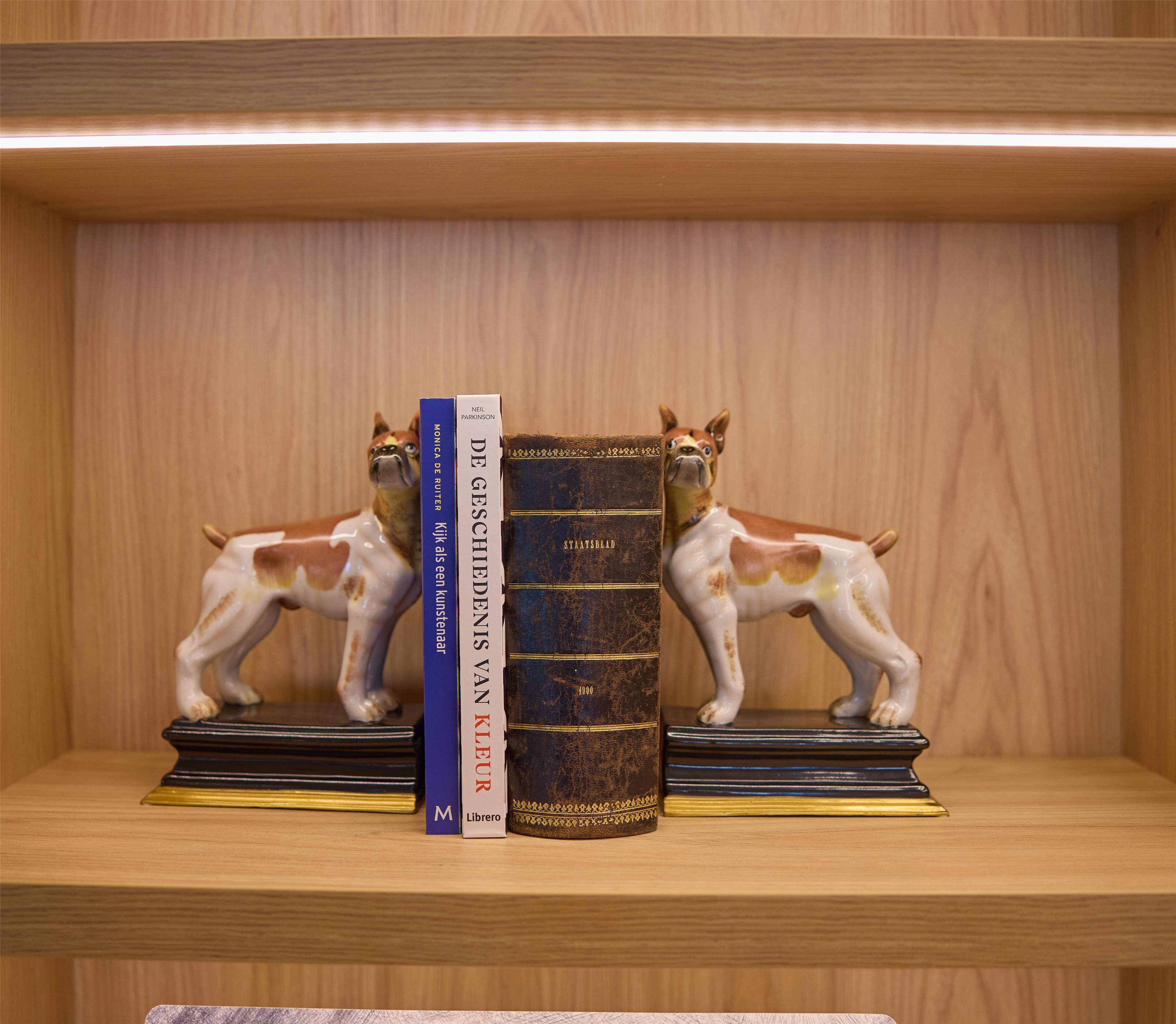 A wooden shelf with three books and two ceramic dog figurines.