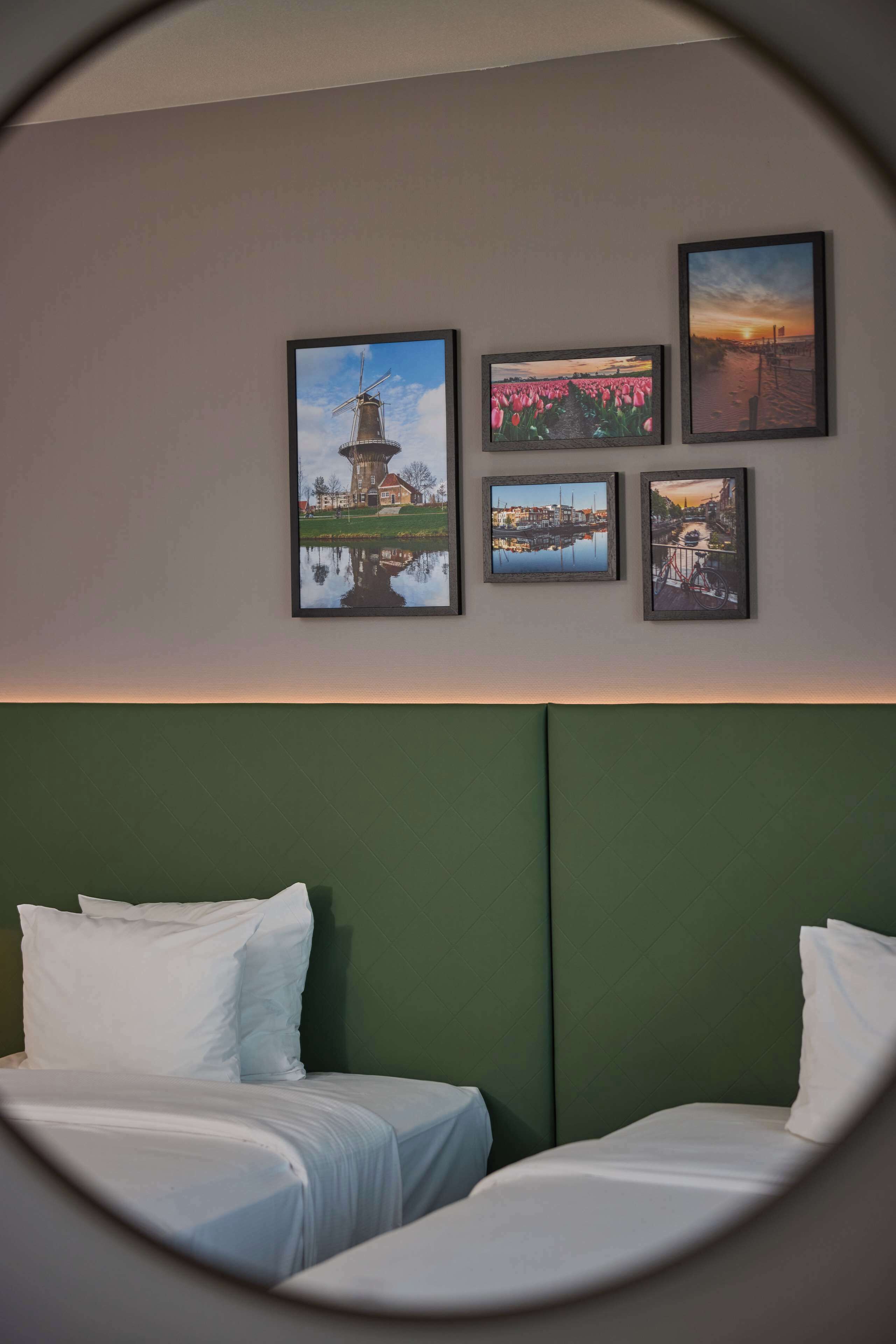 A hotel room with two beds, a green headboard, and four framed pictures on the wall.